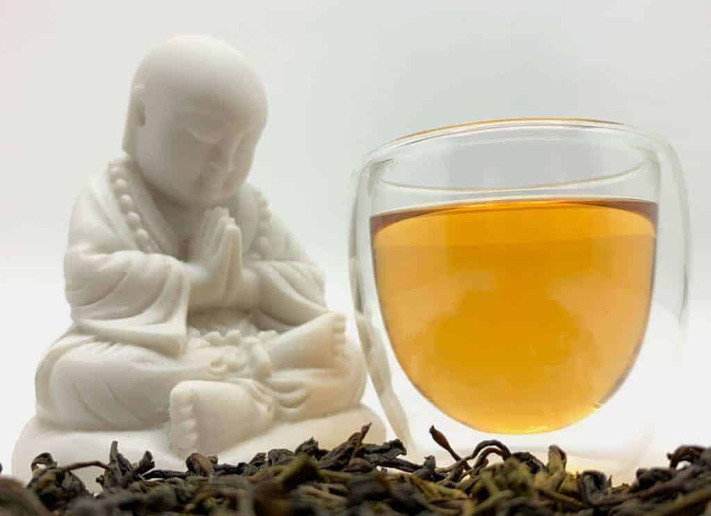 Tea Pet de buda, um copo de chá e folhas de chá espalhadas