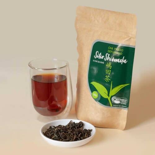 O chá preto inficionado em um copo de vidro duplo, as folhas de chá em um pequeno recipiente e a embalagem do chá.