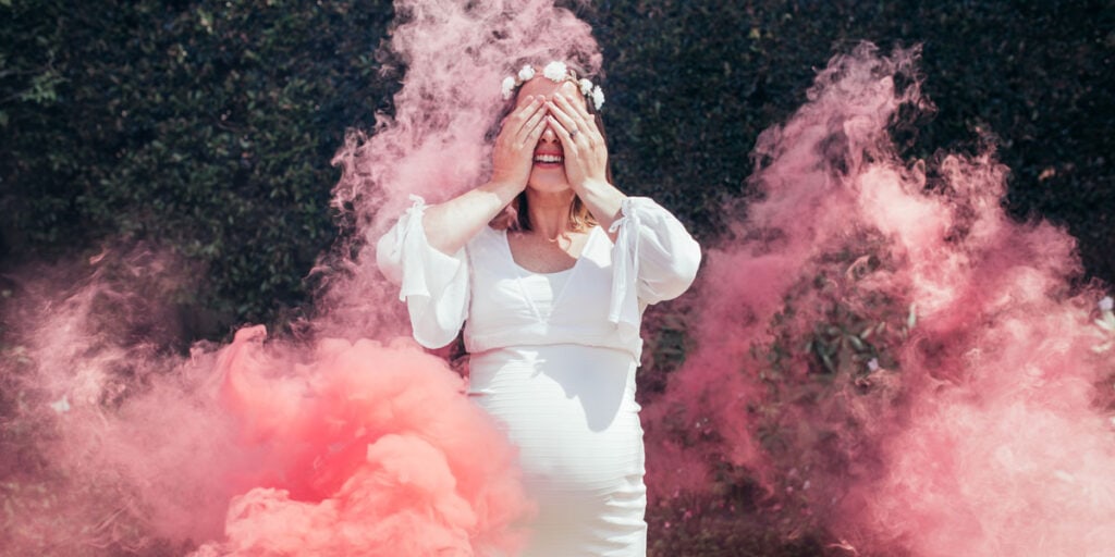 Mulher grávida sendo surpreendida com fumaça rosa em seu chá revelação.